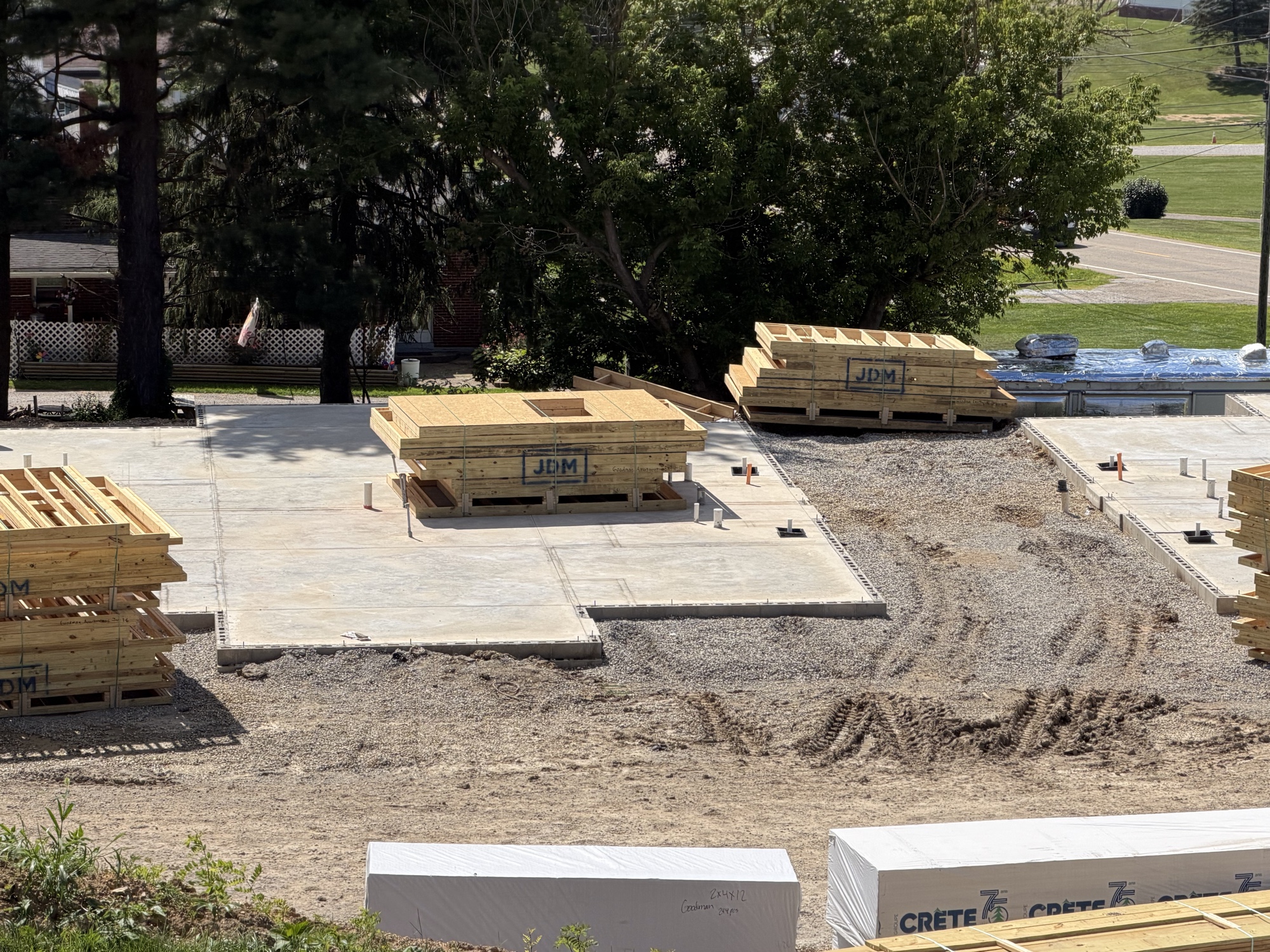 Real construction photo: floor truss bundles staged across the completed foundation slabs with anchor bolts visible along the perimeter at The Legacy at Richland Commons, July 30, 2026