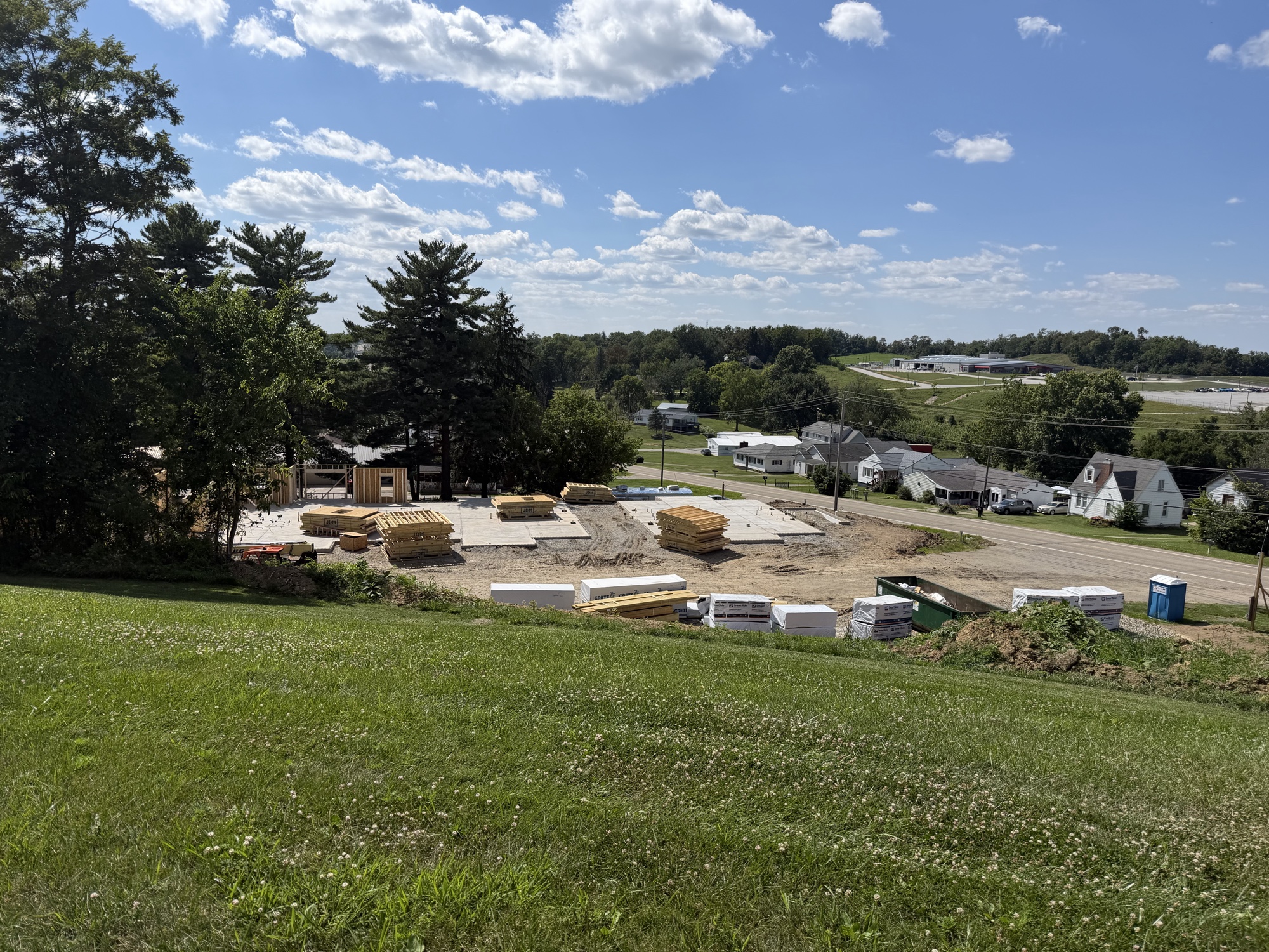 Real construction photo: wide site view of The Legacy at Richland Commons showing the completed foundation pad with framing materials staged for installation, July 30, 2026